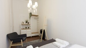 A modern bedroom with a bed, a chair, a dresser, a mirror, and a standing fan.