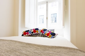 A bed with a patterned pillow and a plain white bedspread in a room with a window. - Downtown Classic by Homing (Lisbon)