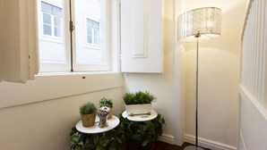 A corner with a window, a white door, a floor lamp, and two small tables with potted plants.