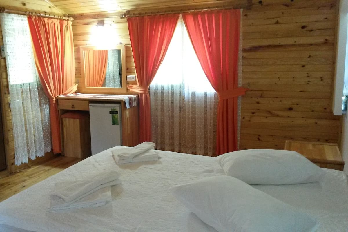 Quarto de cabana de madeira com cama, escrivaninha pequena e geladeira.