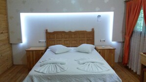 A neatly made bed with a wooden headboard, two bedside tables, and a wall-mounted light fixture. - Hotel Yavuz Bungalow (Kemer)