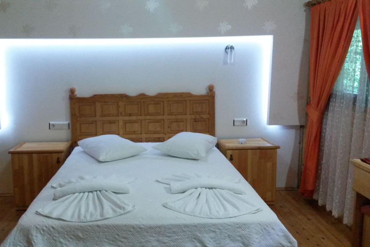 Cama bem arrumada com cabeceira de madeira, duas mesas de cabeceira e luminária fixada na parede.