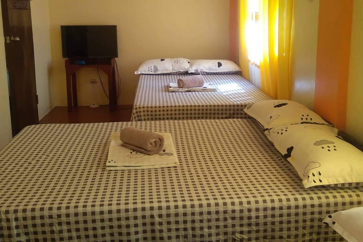 A hotel room with a checkered bedspread, a television on a stand, and a window with yellow curtains.