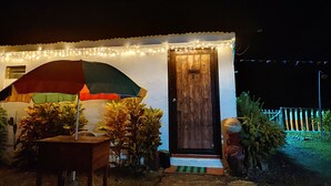 Una casita con puerta de madera, un porche con un paraguas colorido y luces colgantes.