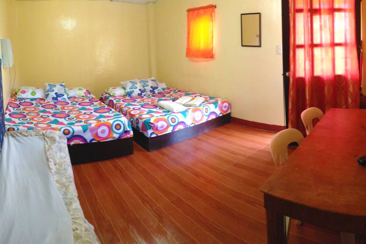 A room with two beds, a wooden floor, a TV, and a table.