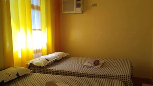 Habitación con dos camas, cada una con una colcha a cuadros y almohadas con motivos de nubes. Se observa un equipo de aire acondicionado fijado en la pared.