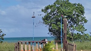 Una valla de madera con franjas anaranjadas y blancas, un árbol y un cielo azul despejado.