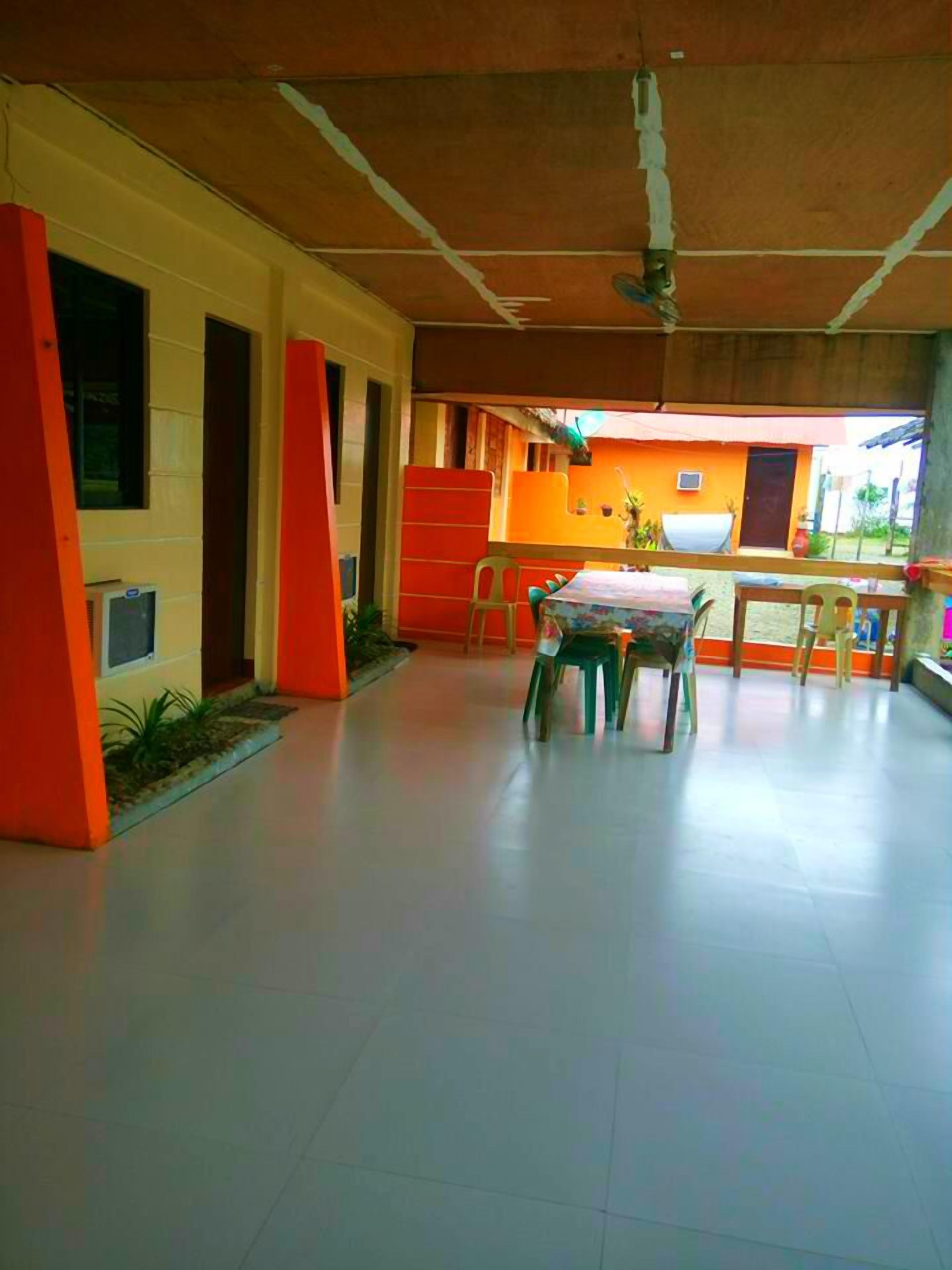 A spacious indoor area with a high ceiling, a dining table with chairs, and a view of an orange building outside.