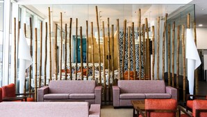 Un hall d’entrée moderne doté d’espaces de détente, d’une cloison en verre agrémentée d’éléments verticaux en bambou et d’un mur à motifs en arrière-plan.