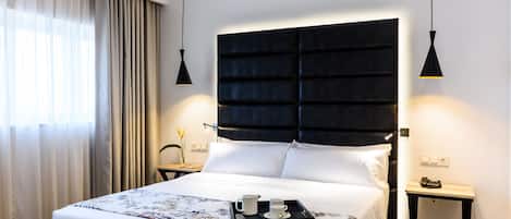 A neatly made bed with a black headboard, a bedside table with a lamp, and a tray with a cup and saucer on the bed.
