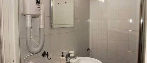 Un baño con un lavamanos blanco, espejo y secador de pelo en la pared.