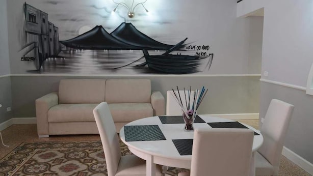 A modern living room with a sofa, a dining table with chairs, a decorative wall mural, and a patterned rug. - B&B La Torretta di Chiaia (Naples)