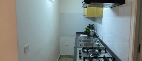 A compact kitchen with a gas stove, a sink, and a wooden cabinet above the stove.