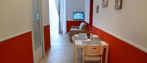 Um corredor com área de jantar, incluindo uma mesa, cadeiras, um sofá e uma televisão fixada na parede.