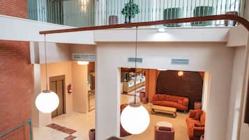 Un vestíbulo de hotel con una escalera, un área de descanso con sofás y una cocina visible al fondo.