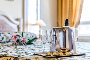 A table with a floral tablecloth, two glasses, a silver decanter, and chocolates on a tray. - Roma Aurea (Talavera de la Reina)