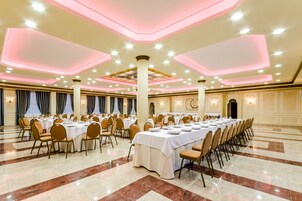 Un amplio salón de banquetes con varias mesas redondas dispuestas para cenar, con suelo de mármol pulido y un techo alto con iluminación empotrada.