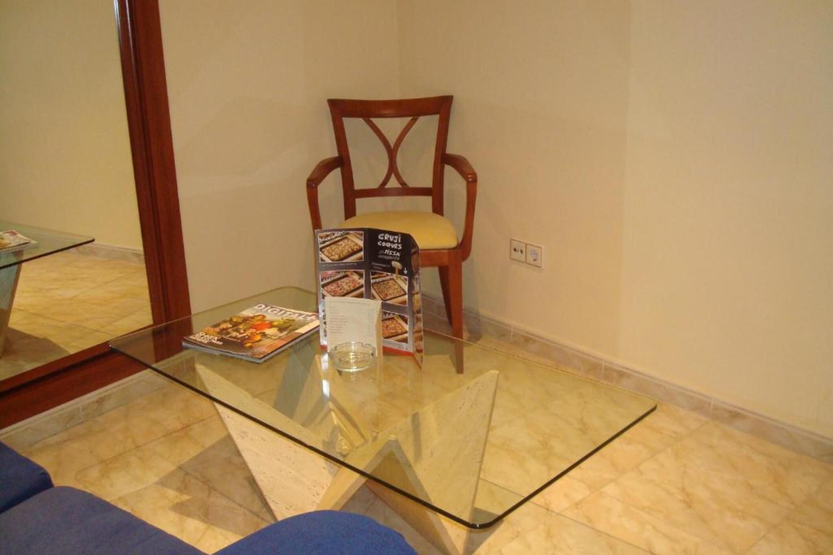 A glass-top table with a chair and a brochure stand in a room with a tiled floor.