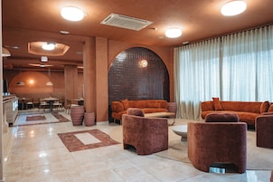 Un interior moderno con una zona de estar que incluye sofás y sillones, una zona de comedor con mesas y sillas, y un amplio ventanal con cortinas.