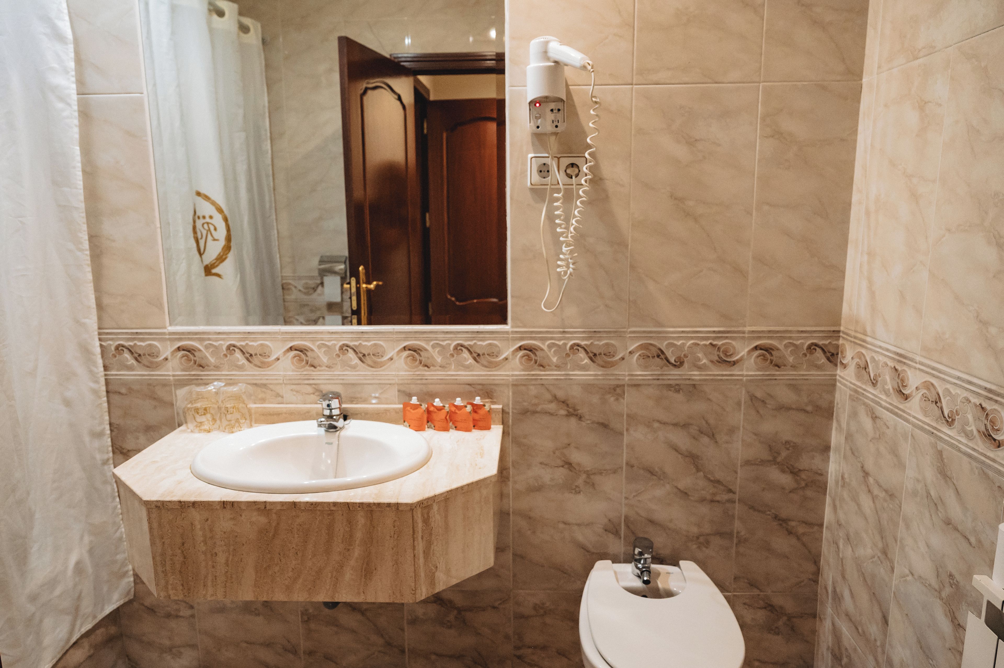 A bathroom with a marble sink, a toilet, and a hairdryer mounted on the wall.