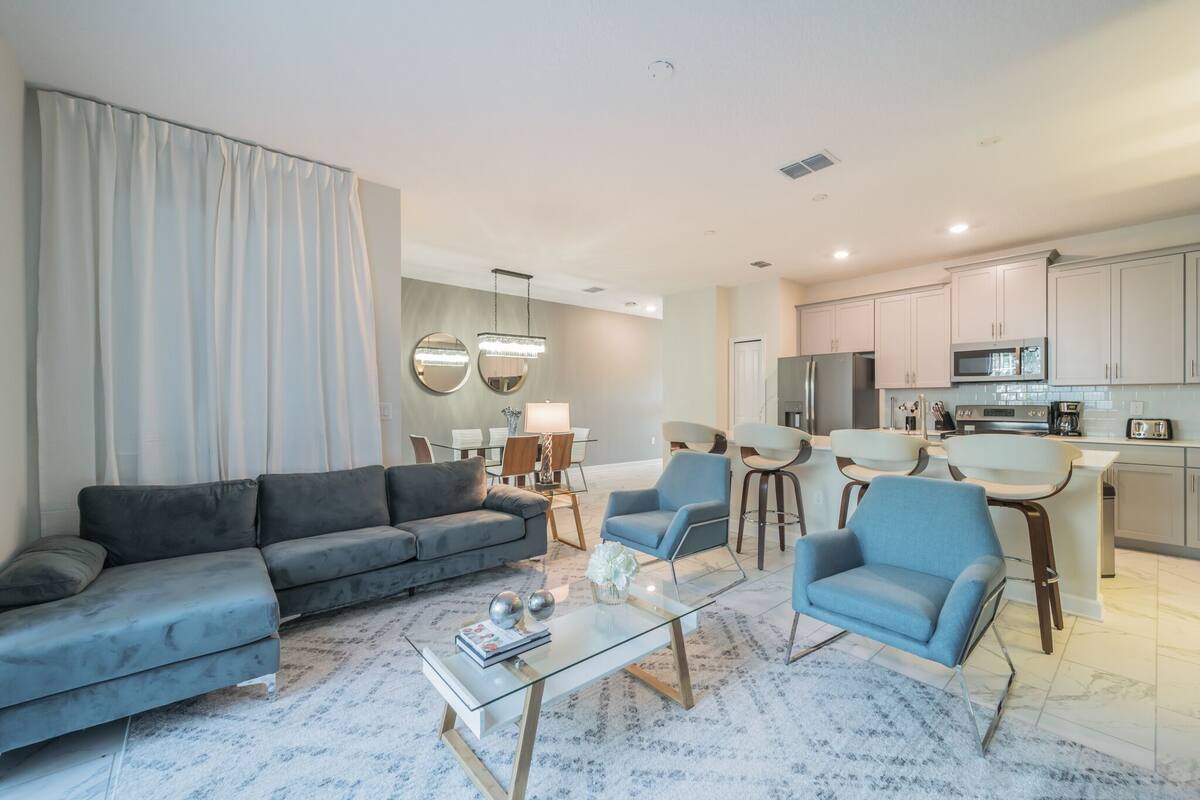 A modern living room with a sectional sofa, a glass coffee table, and a dining area with chairs.