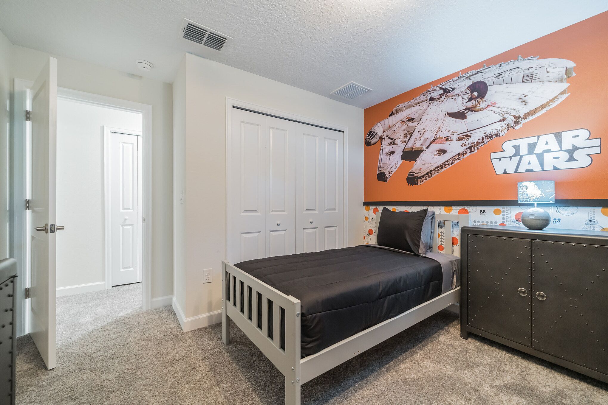 A bedroom with a Star Wars-themed wall, a bed, a wardrobe, and a door.
