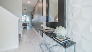 A modern hallway with a marble floor, a console table with a vase of flowers, a book, and a lamp. - Insight Hospitality (Davenport)