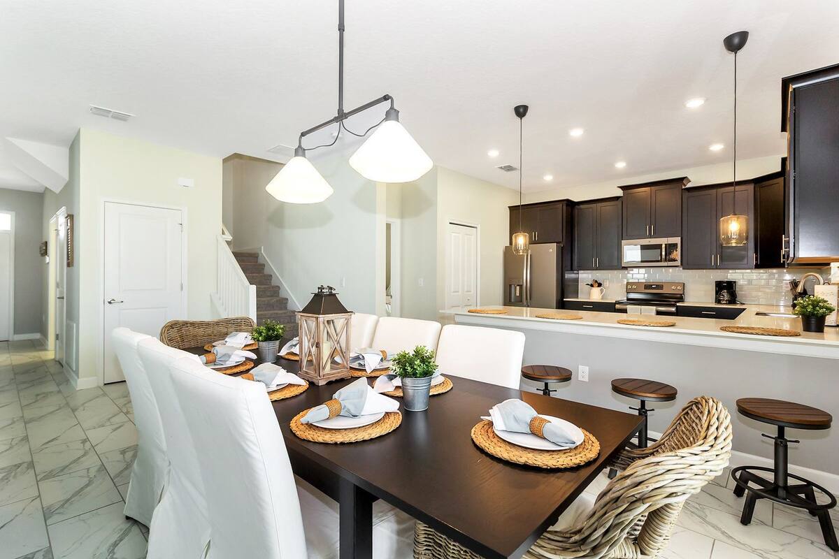 A modern kitchen with dark cabinets, a central island, and a dining area with a dark wooden table set for four.