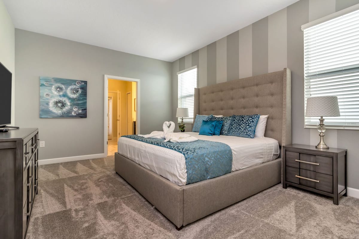 A bedroom with a large bed, a nightstand, a dresser, and a painting on the wall.