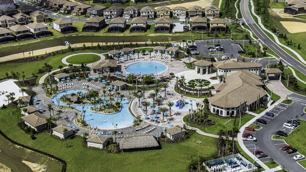 An aerial view of a resort with multiple swimming pools, a parking area, and residential buildings. - Insight Hospitality (Davenport)