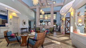 A spacious lobby with high ceilings, wooden beams, and a central seating area with wicker chairs and a coffee table. - Insight Hospitality (Davenport)