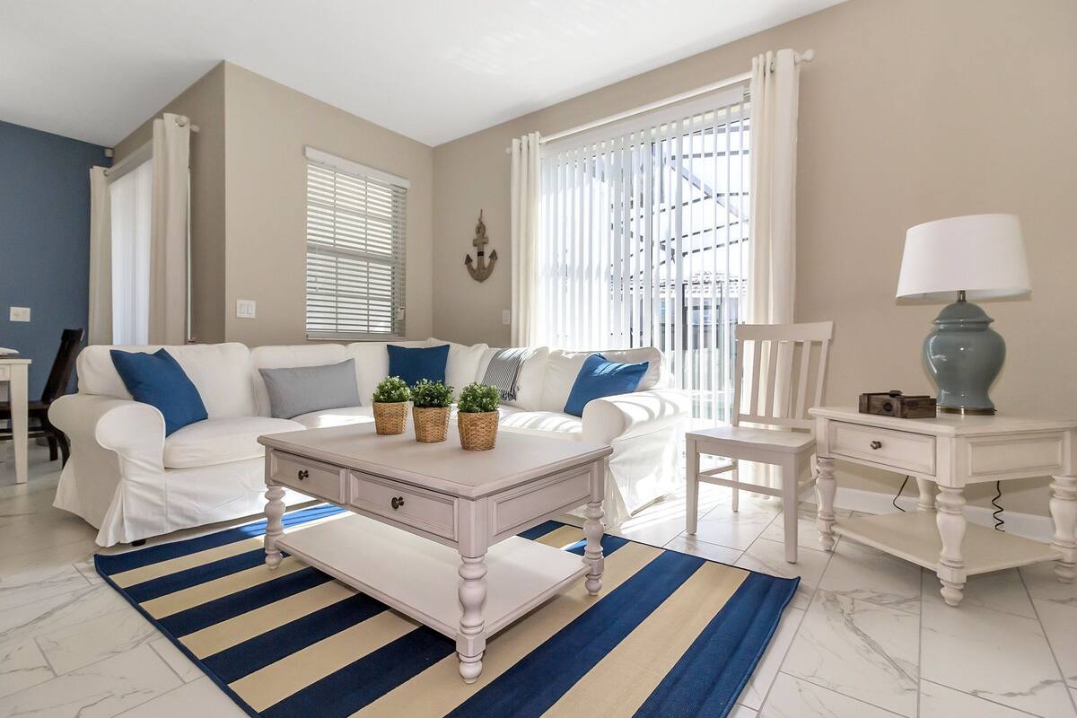 A living room with a white sofa, blue cushions, a white coffee table, and a striped rug.