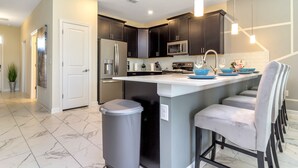 A modern kitchen with dark cabinets, stainless steel appliances, and a central island with bar stools. - Insight Hospitality (Davenport)
