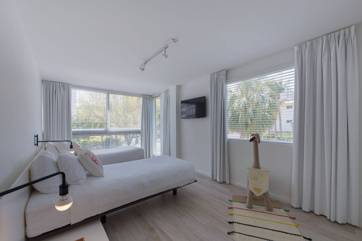 A modern bedroom with a bed, a mounted TV, and large windows with curtains.