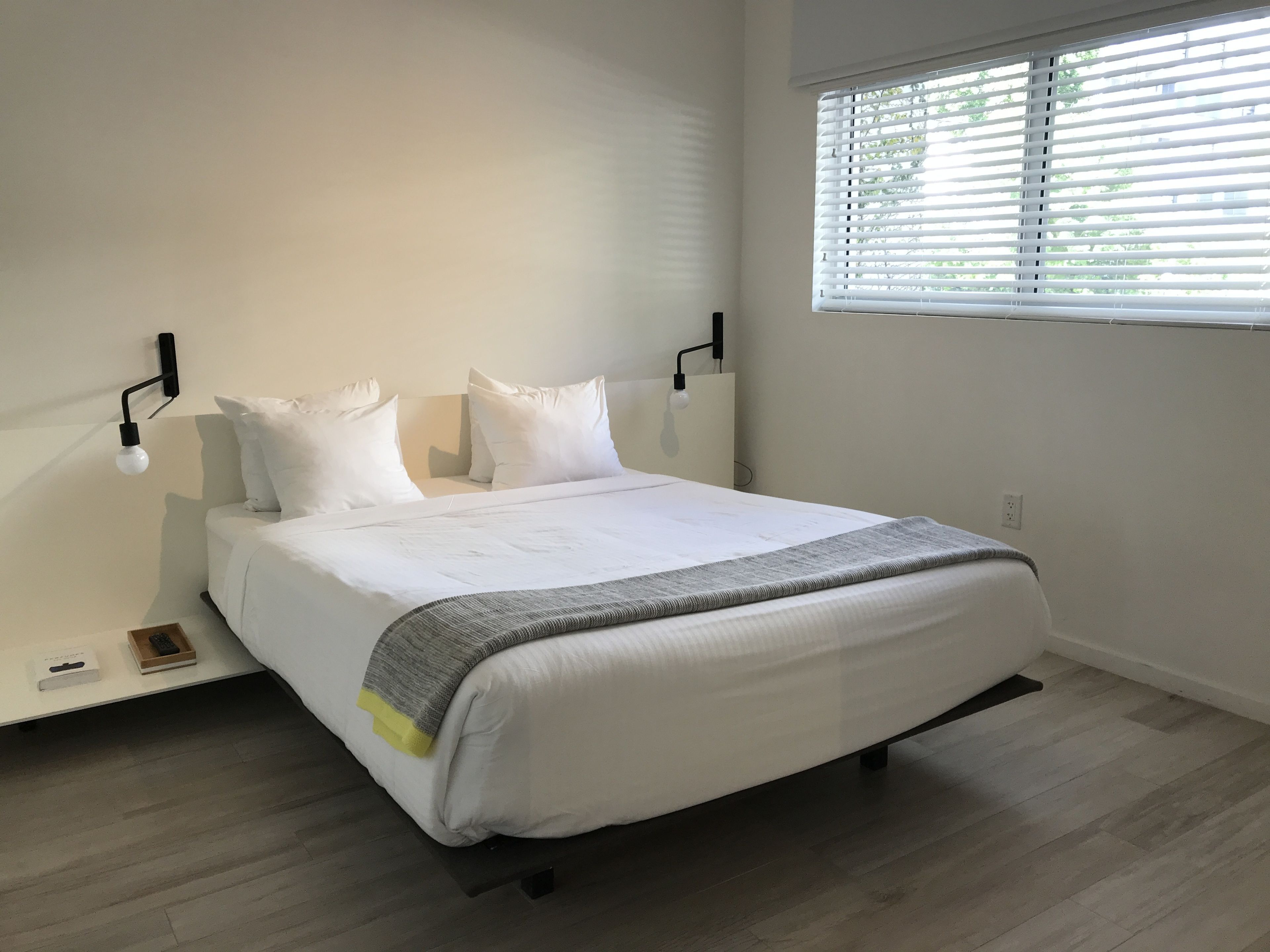 A modern bedroom with a large bed, white bedding, and a window with blinds.