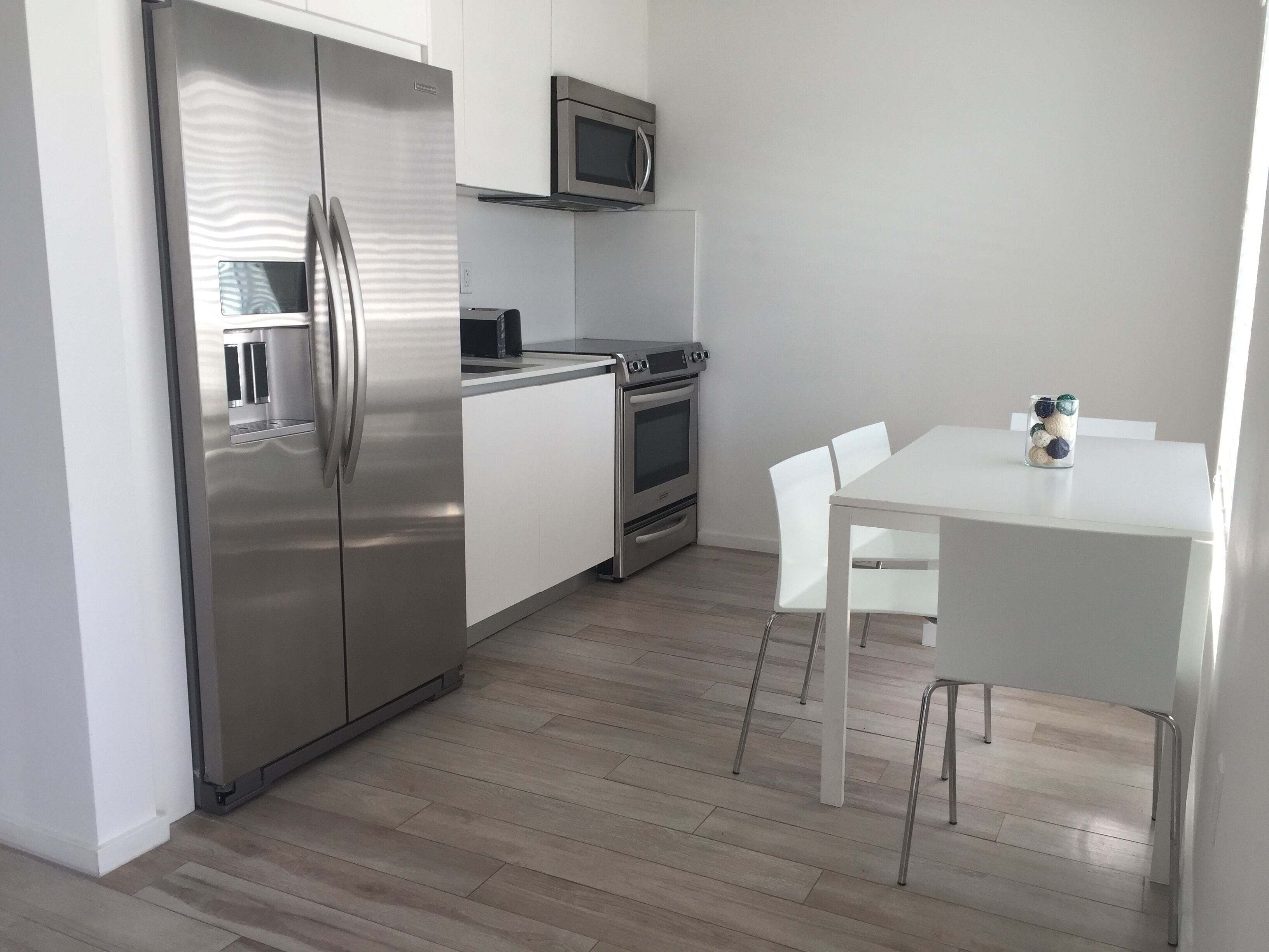 A modern kitchen with stainless steel appliances, a microwave, and a dining area with white chairs and a table.