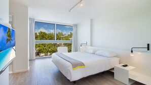 A modern bedroom with a large bed, a bedside table, a TV, and a window with blinds. - Beach Haus Key Biscayne (Key Biscayne)