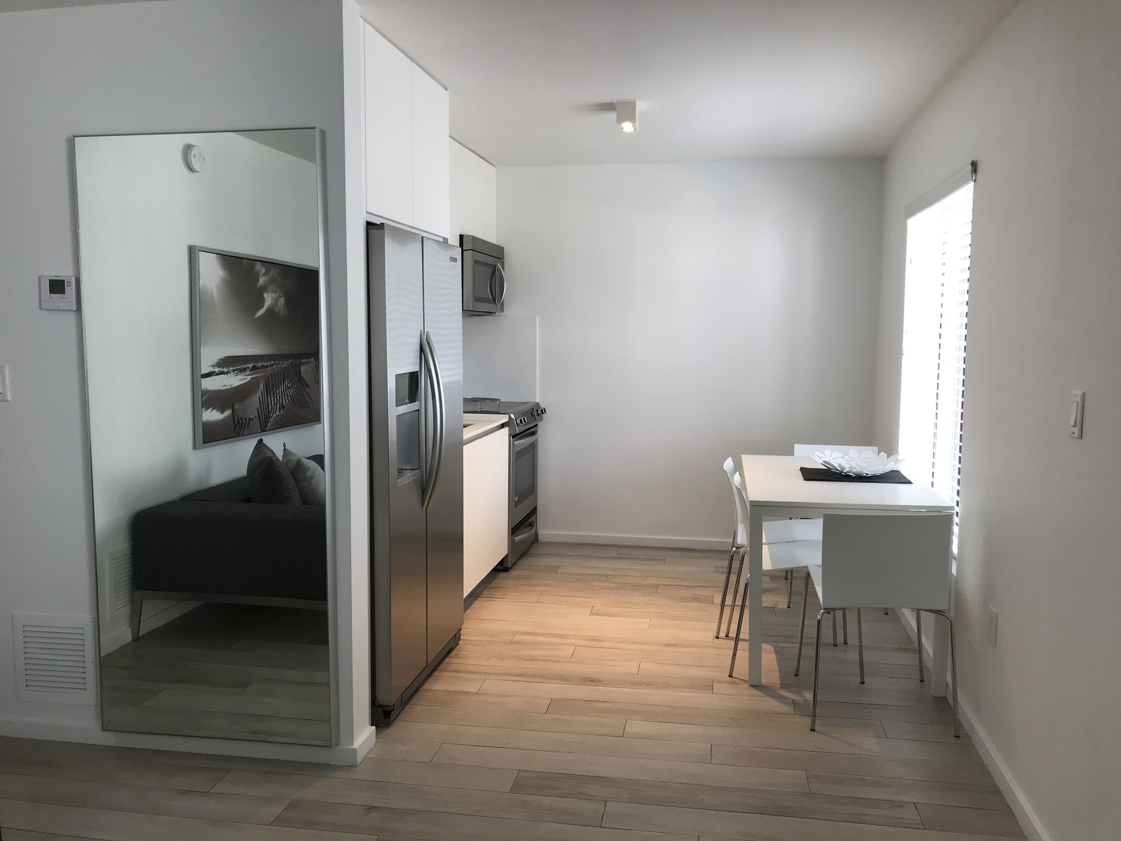 A compact kitchen with a refrigerator, oven, and microwave. There's a dining table with chairs and a window with blinds.