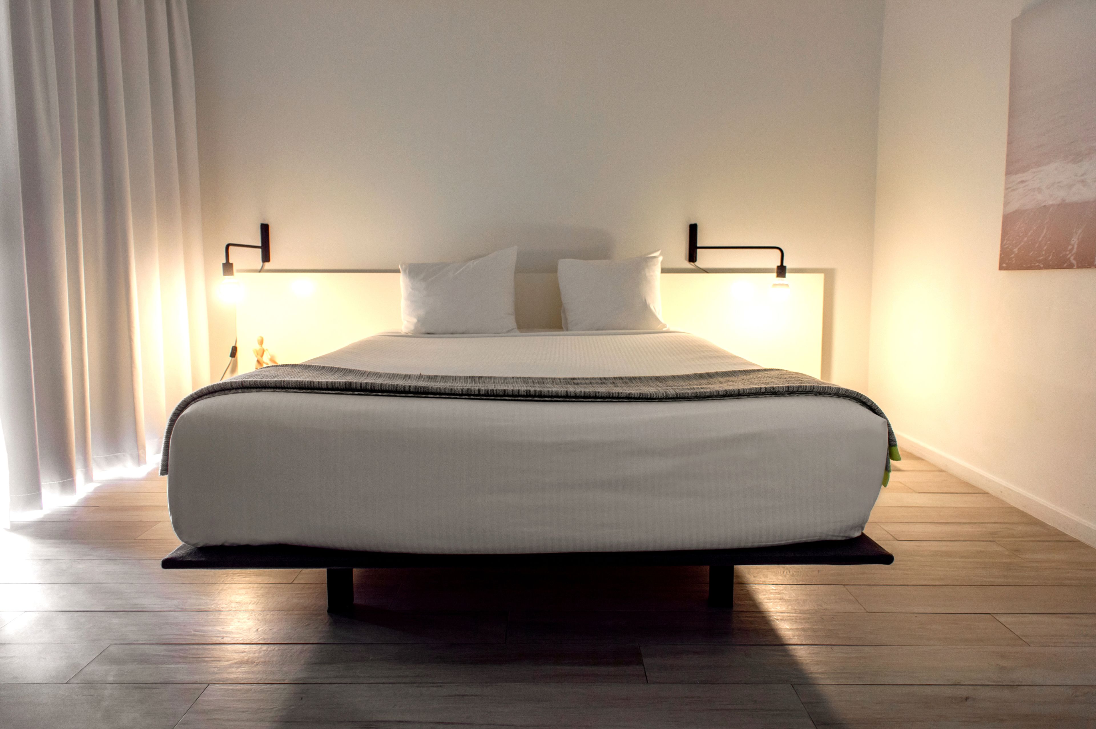 A modern bedroom with a large bed, two bedside lamps, and a view of the ocean through the window.