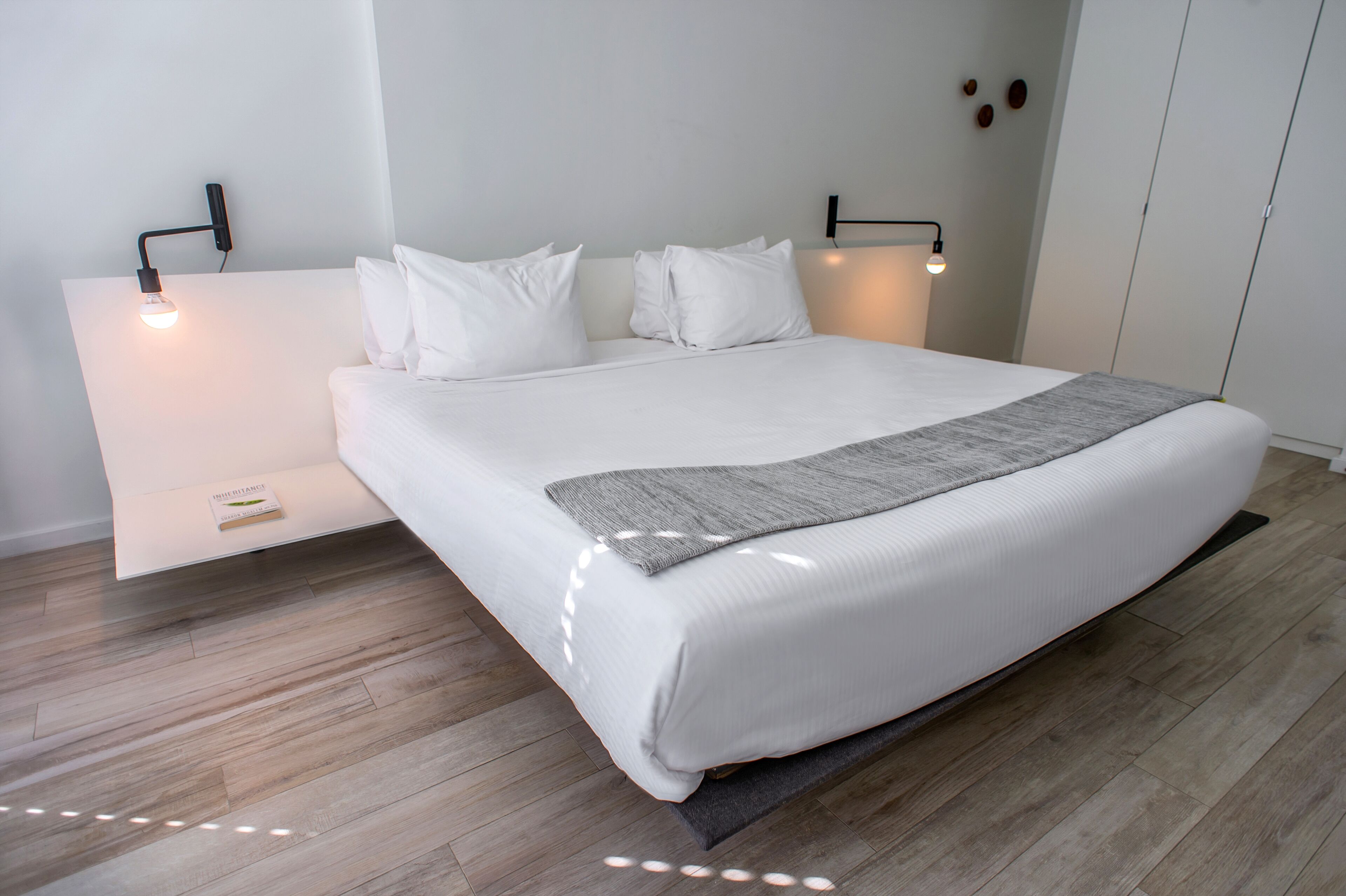 A modern bedroom with a large bed, white bedding, and two wall-mounted reading lamps.