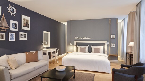 A modern hotel room with a bed, a desk, a sofa, and a chair. - Hapimag Resort Hamburg (Hamburg)