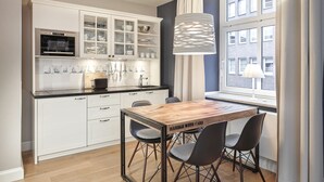 A modern kitchen with white cabinetry, a built-in oven, and a dining area with a wooden table and chairs. - Hapimag Resort Hamburg (Hamburg)