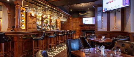 A bar area with wooden furnishings, bar stools, and a television displaying news.