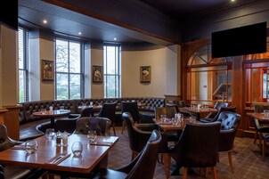 Um restaurante com assentos de couro, mesas de madeira e cadeiras pretas.