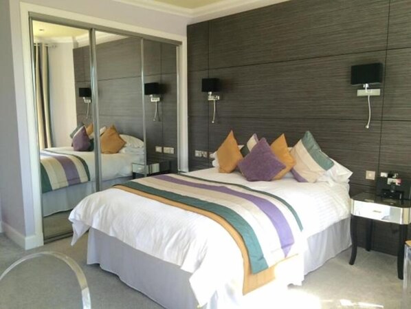 A hotel room with a large bed, a mirror, a dark wood-paneled wall, and a small bedside table with a lamp. - The Ferryhill House Hotel (Aberdeen)