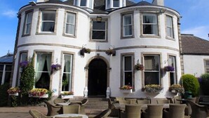 A white building with a curved facade, multiple windows, and outdoor seating area with wicker furniture. - The Ferryhill House Hotel (Aberdeen)