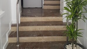 Una escalera con peldaños de mármol, paredes blancas y plantas en macetas.