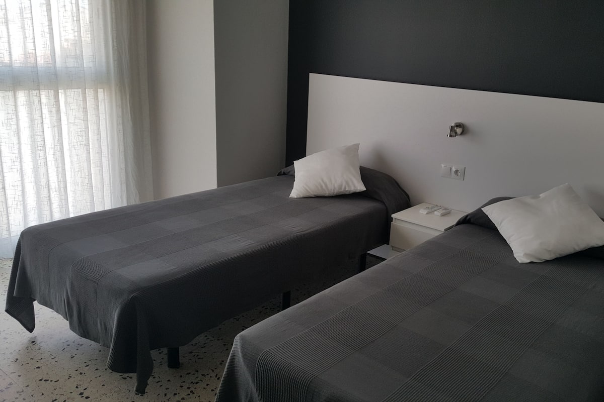 Une chambre d’hôtel avec deux lits simples, une table de chevet et une prise de courant.