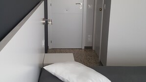 Un pasillo estrecho que termina en una cama, con dos almohadas blancas.