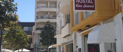 A hostel named "Can Jojanet" with a yellow facade, outdoor seating, and a clear sky.